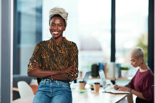 Cropped portrait of an attractive young businesswoman sitting on the desk in her office while her colleague works behind her